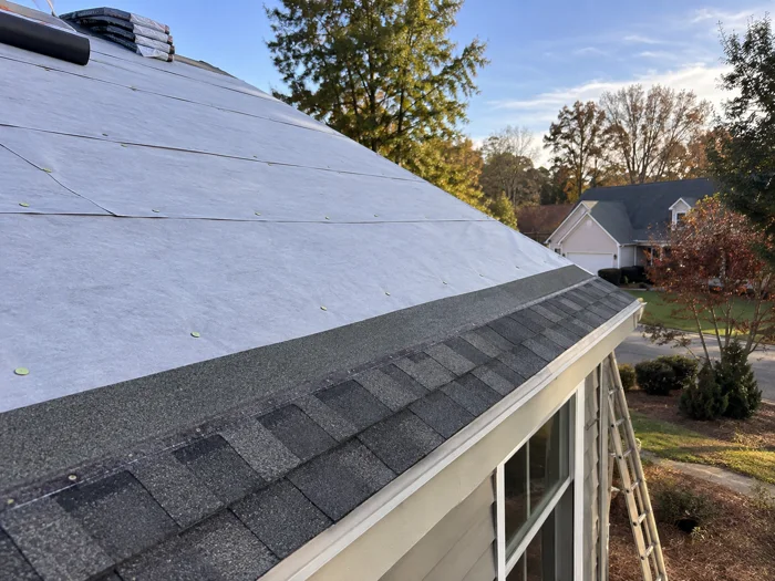 A roof deck with new underlayment rolled out and the first course of shingles started at the eave, no people